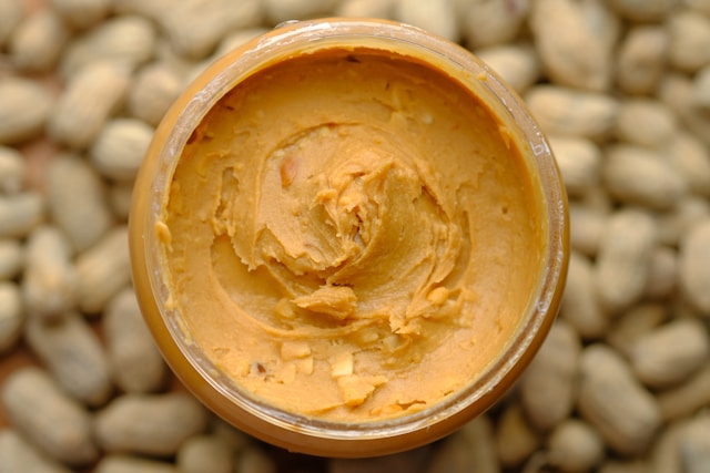 Jar of peanut butter sitting on raw peanuts